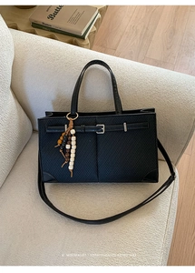 Detail der schwarzen Tote-Tasche mit Perlenanhänger auf einem beigen Sofa