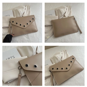 Détail de pochette enveloppe beige avec œillets argentés et dragonne sur tissu blanc