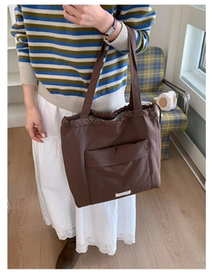 Detail view of large dark brown drawstring tote bag with exterior pocket worn on shoulder