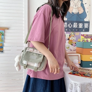 Close-up of olive green canvas crossbody bag with multi-pocket storage and cute plush charm