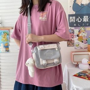 Detail of grey and white canvas crossbody bag featuring a plush charm and fashion label