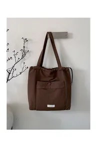 Detail of a brown drawstring tote bag with a front pocket and white woven brand label