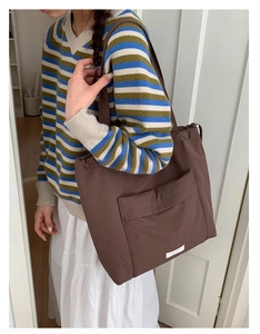 Detail view of brown drawstring tote bag featuring front flap pocket and white label