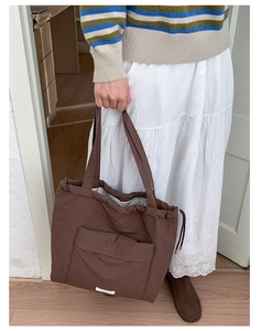 Detail of a brown drawstring tote bag in nylon fabric with front pocket and soft texture