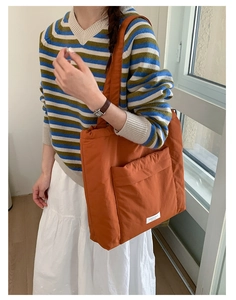 Detail of an orange quilted tote bag with a minimalist front pocket on a casual striped sweater