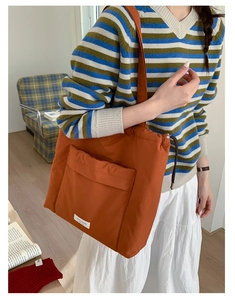 Close-up of orange drawstring tote bag featuring front flap pocket and woven label