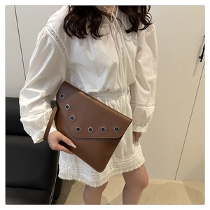 Détail d'une pochette enveloppe marron avec œillets métalliques argentés et dragonne chic