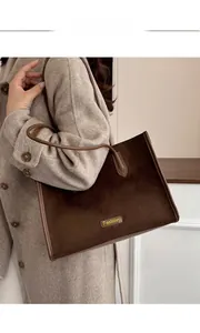 Detail of dark brown suede tote bag with leather trim worn over a beige coat