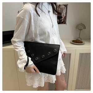 Détail d'une pochette enveloppe en cuir noir avec des œillets métalliques et une dragonne