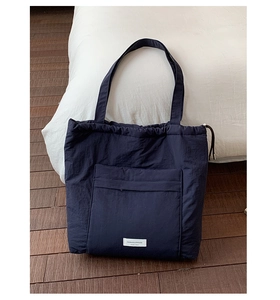 Detail of navy blue nylon tote bag with drawstring closure and woven brand label