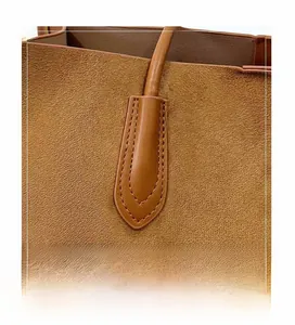 Macro detail of the reinforced double stitching on brown suede tote bag handles