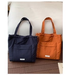Detail of drawstring tote bags in navy and orange featuring front pockets and woven labels