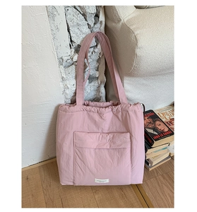 Detail of a pink puffy tote bag with drawstring closure and brand label on a front pocket