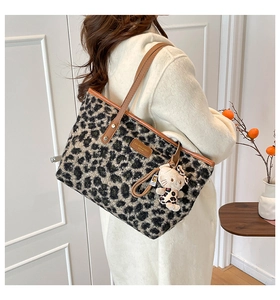 Detail shot of leopard print tote bag with brown leather trim and plush kitty charm