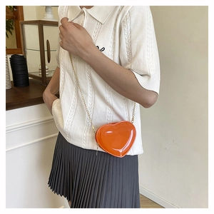 Detail einer leuchtend orangefarbenen Mini-Kettentasche in Herzform als modisches Accessoire