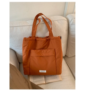 Detail shot of a burnt orange puffy tote bag on a sofa featuring a large front pocket