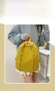Model wearing a yellow nylon backpack with multi-pocket design in a cozy indoor setting