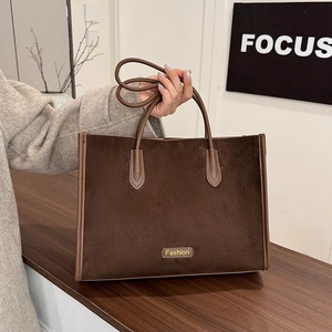 Detail of coffee suede tote bag with brown leather handles and Fashion logo on wooden table