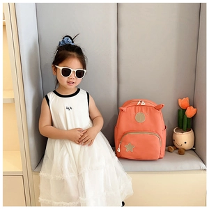 Detail of coral orange kids backpack with cute ears and star patch on model girl
