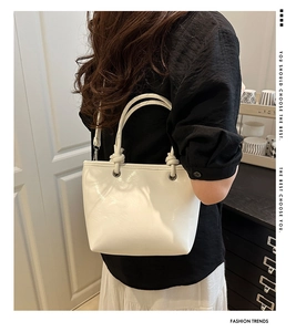 Detail of white glossy leather tote bag with knotted handles and adjustable shoulder strap