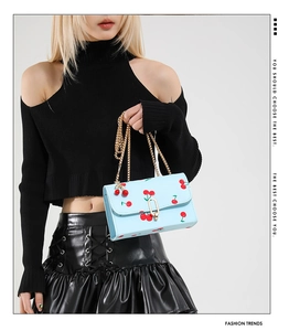 Detail of light blue mini chain bag with red cherry prints and golden metal buckle