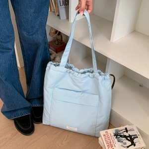 Light blue quilted puffer tote bag with drawstring closure and large front pocket on blue denim