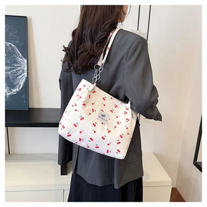 Close-up of a white canvas tote bag with cherry prints and a stylish silver metal chain strap
