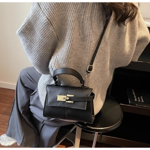Detailed view of black pebbled leather texture and gold twist-lock buckle on top handle bag