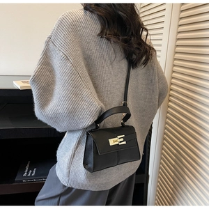 Detail of black textured leather bag with gold buckle shown on person for size scale