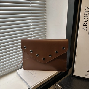 Sac enveloppe en cuir marron avec œillets métalliques sur un décor de studio sobre