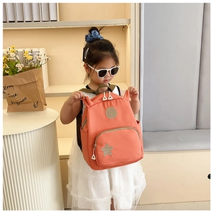 Detail view of the orange-pink school bag with cartoon ears and star patch on a young model
