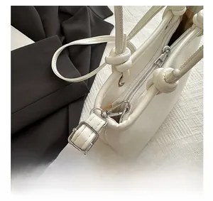 Detail view of white leather bucket bag with silver zipper and knot shoulder strap detail