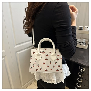 Detail showing cherry print pattern, round handles and lace edge on the white crossbody bag