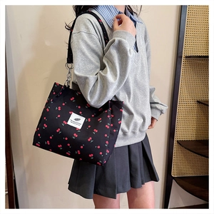 Detailed view of black canvas tote bag featuring red cherry prints and metal chain strap