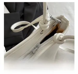 Detail of white leather bucket bag featuring top zipper closure and knot strap design
