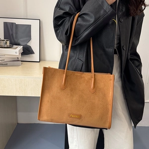 Detail of a brown suede tote bag with metal Fashion logo and long shoulder handles