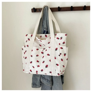 Dettaglio della borsa tote in velluto bianco con stampe di fragole rosse e tasche laterali