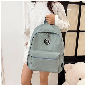 Detail view of light green nylon backpack featuring front zipper pocket and round logo patch