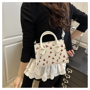 Detail of white cherry print handbag with double handles and metal buckles on shoulder strap