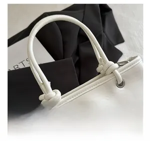 Close-up of white textured leather bucket bag with unique knotted handle and metal eyelet