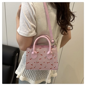 Detail view of pink crossbody bag with red cherry prints shown on a model's shoulder
