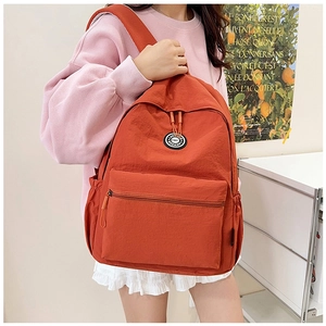 Detailed view of burnt orange nylon backpack featuring round logo and drawstring closure