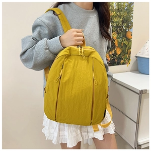 Detail view of yellow lightweight nylon backpack worn by a model in a minimalist home setting