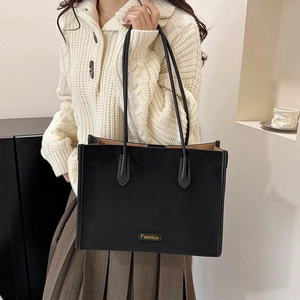 Detail of a large black faux suede tote bag with a gold Fashion metal logo on the front