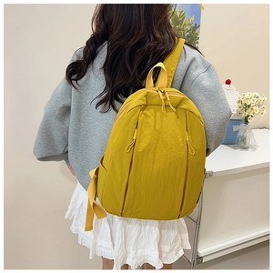 Detail view of yellow nylon backpack with vertical zippers worn by model in home setting
