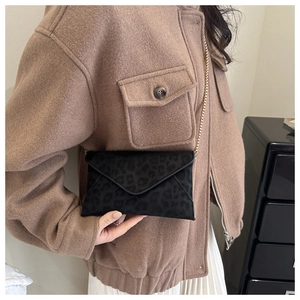 Detail of black leopard envelope bag with gold chain strap on a brown coat
