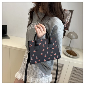Asian model wearing a black square crossbody bag with red cherry prints in a lifestyle setting