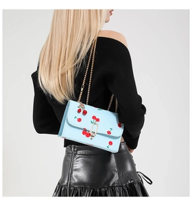 Detail of light blue saddle bag featuring red cherry prints and golden chain strap
