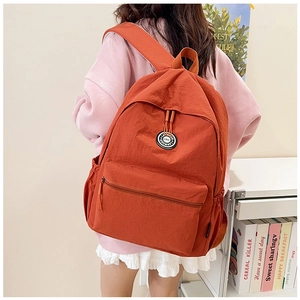 Close-up of orange nylon backpack with front pocket and circular brand logo badge