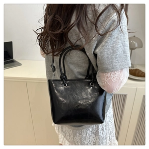 Minimalist black glossy bucket bag worn by a woman in a clean office setting